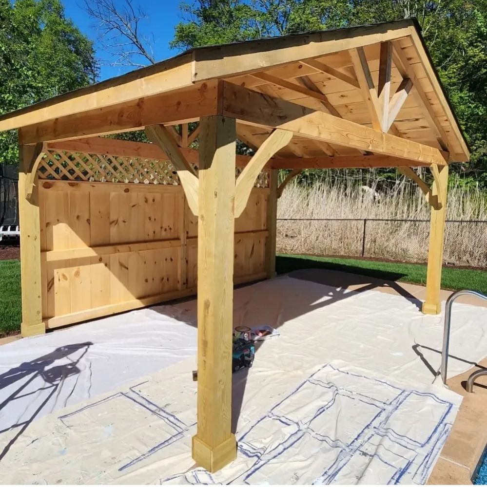 Wooden pergola with a gabled roof and lattice detail, built by a pool on a sunny day.