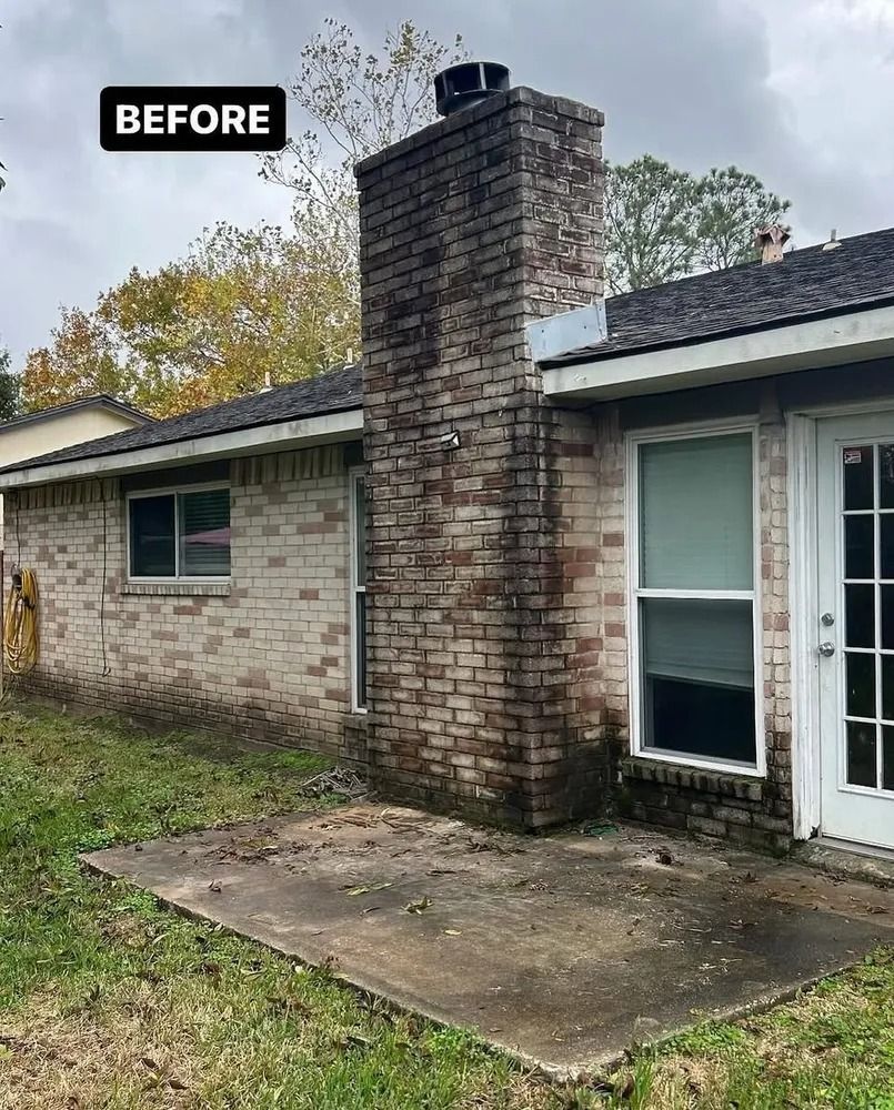 Brick chimney and exterior wall of a house covered in dark mold. A small, gray concrete patio sits in front of the wall.