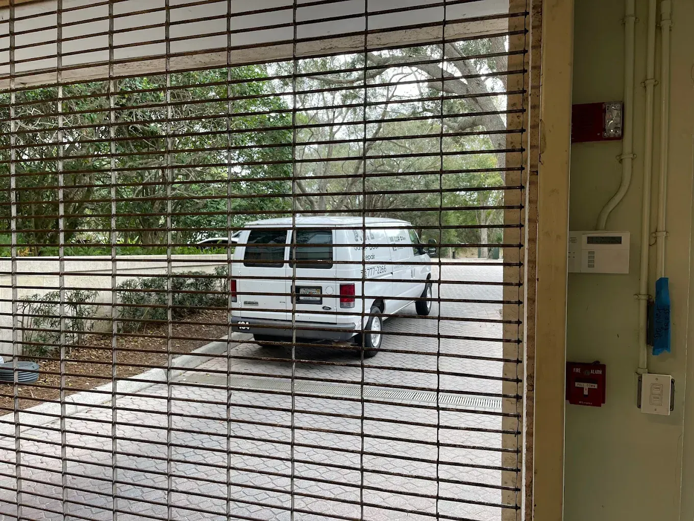 A white van parked outdoors, viewed through a metal security gate.