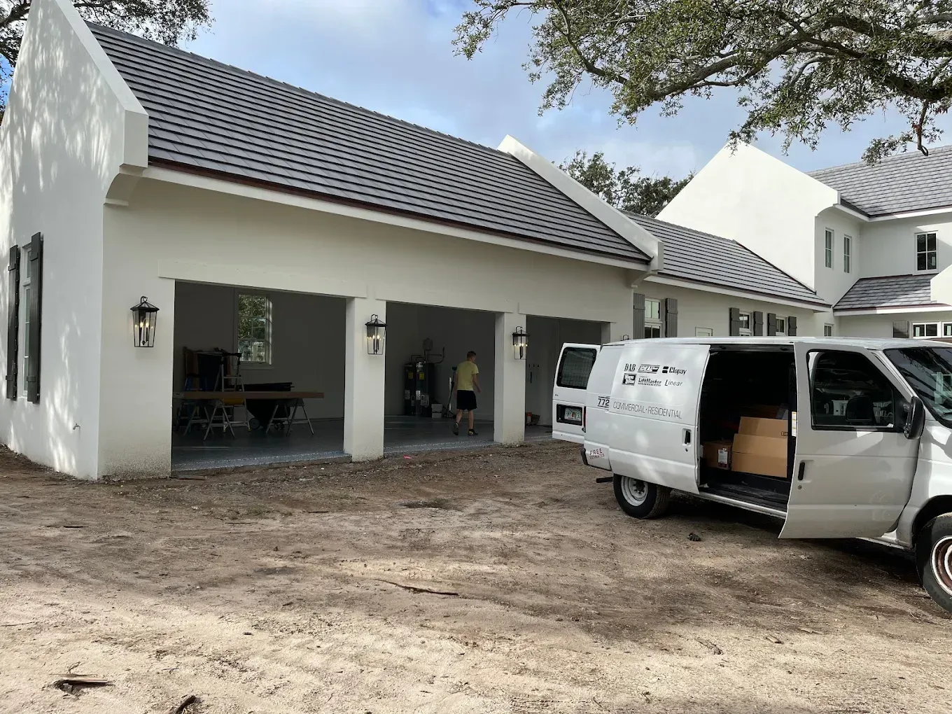 A white van parked next to a modern, three-bay garage with dark roof tiles, with a person standing inside.