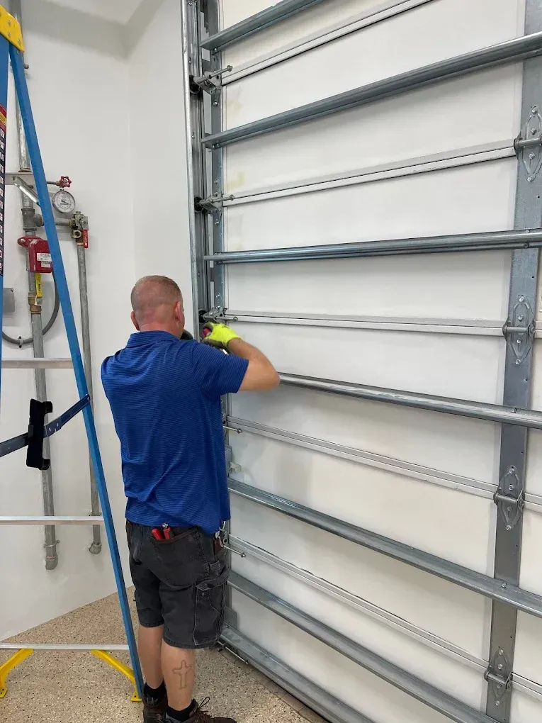 A technician in a blue shirt works on the vertical metal track system of an industrial-style garage door.