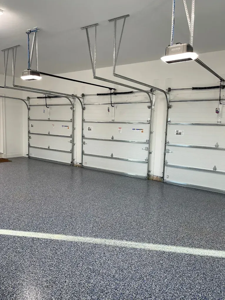 A modern garage interior with speckled flooring and three white garage doors, each equipped with overhead motor systems.