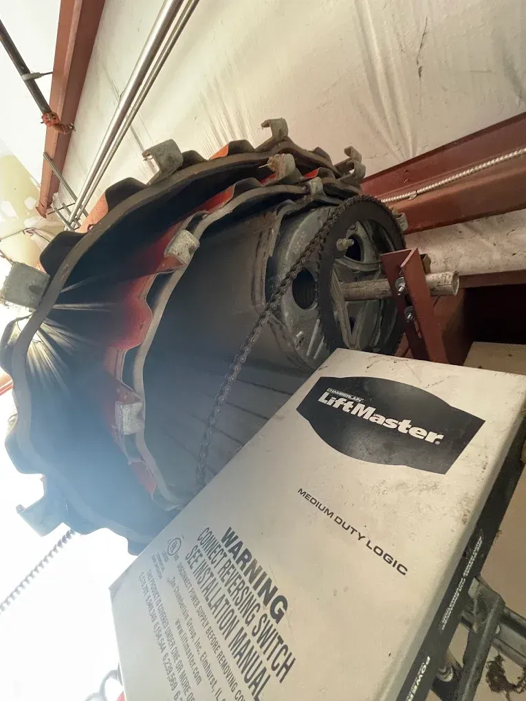 An angled, low-light view of a ceiling-mounted LiftMaster garage door opener mechanism with a belt and pulley system.