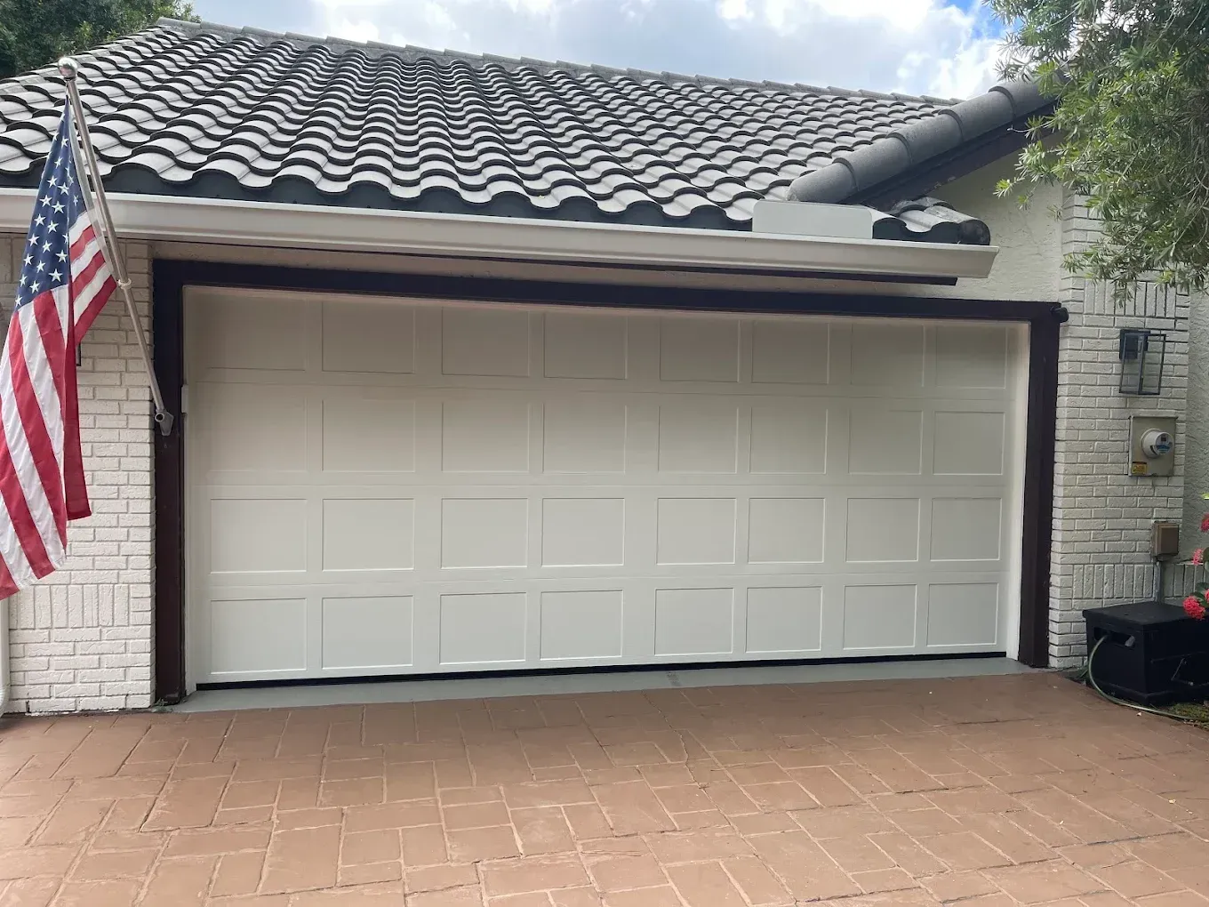 White paneled garage door on a brick house with a tile roof and an American flag hanging on the left side.