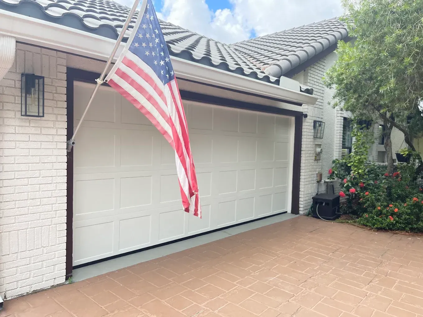 A residential home with a white brick exterior and a white garage door, featuring an American flag mounted near the roof.