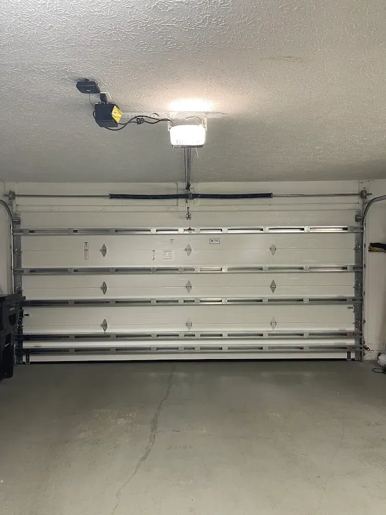 A closed white garage door with a motorized opener mounted on the ceiling in an indoor garage.