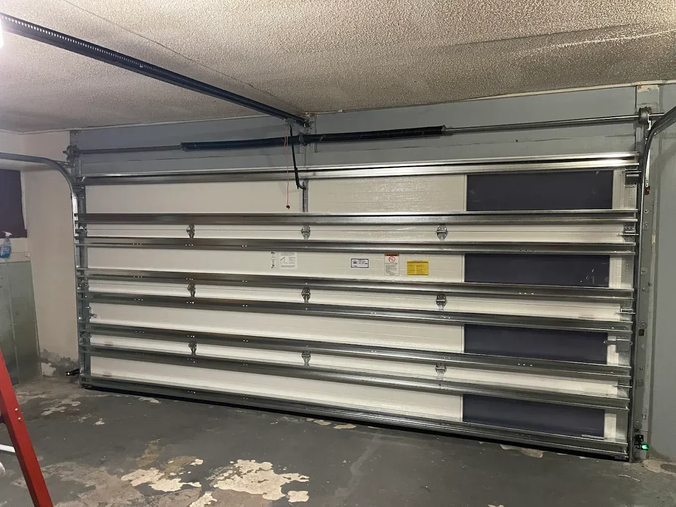 Interior view of a white, multi-paneled garage door with horizontal metal support struts inside a concrete garage.