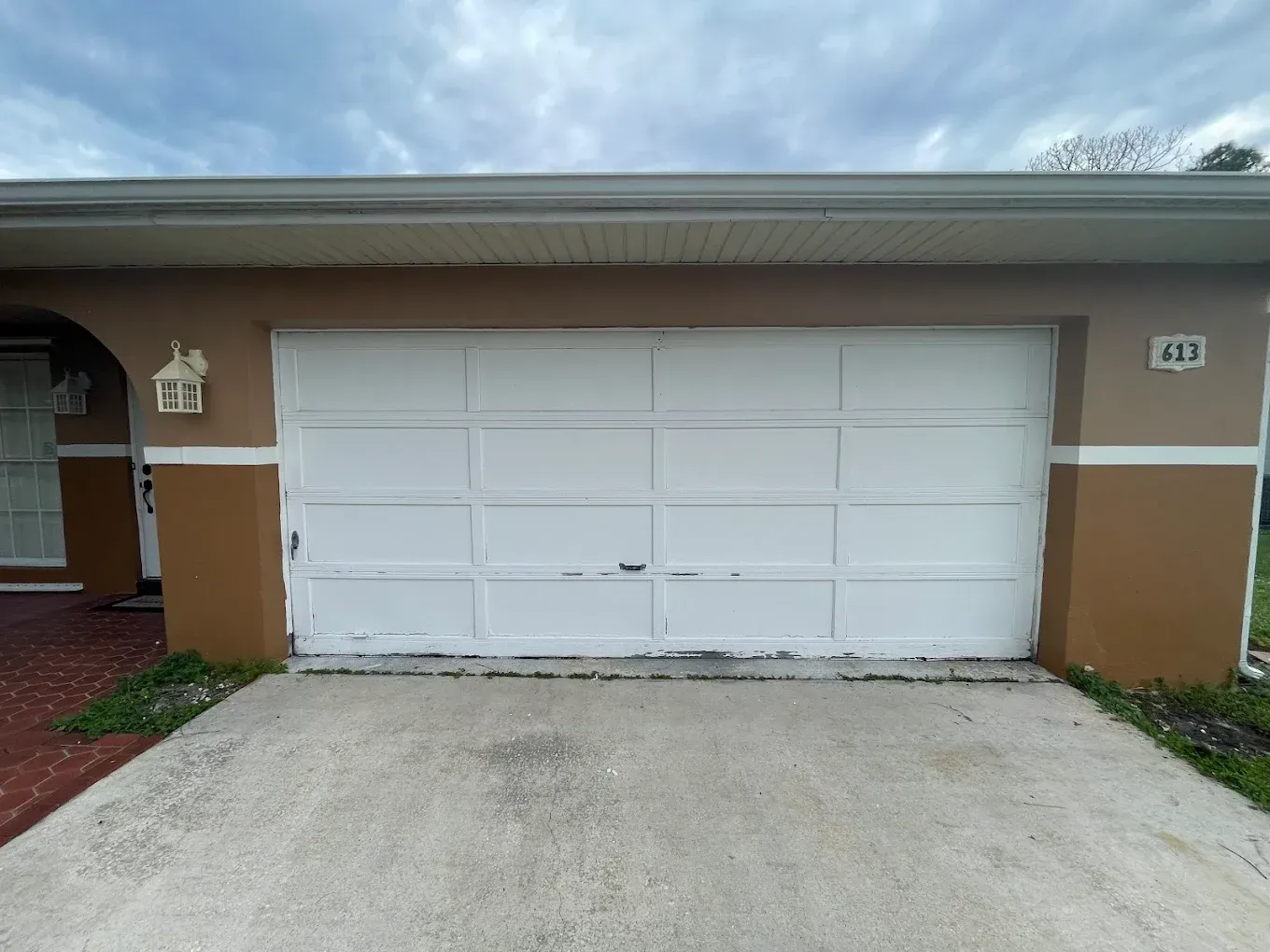 A white, multi-panel garage door on a brown stucco house with a concrete driveway and an address plaque to the right.