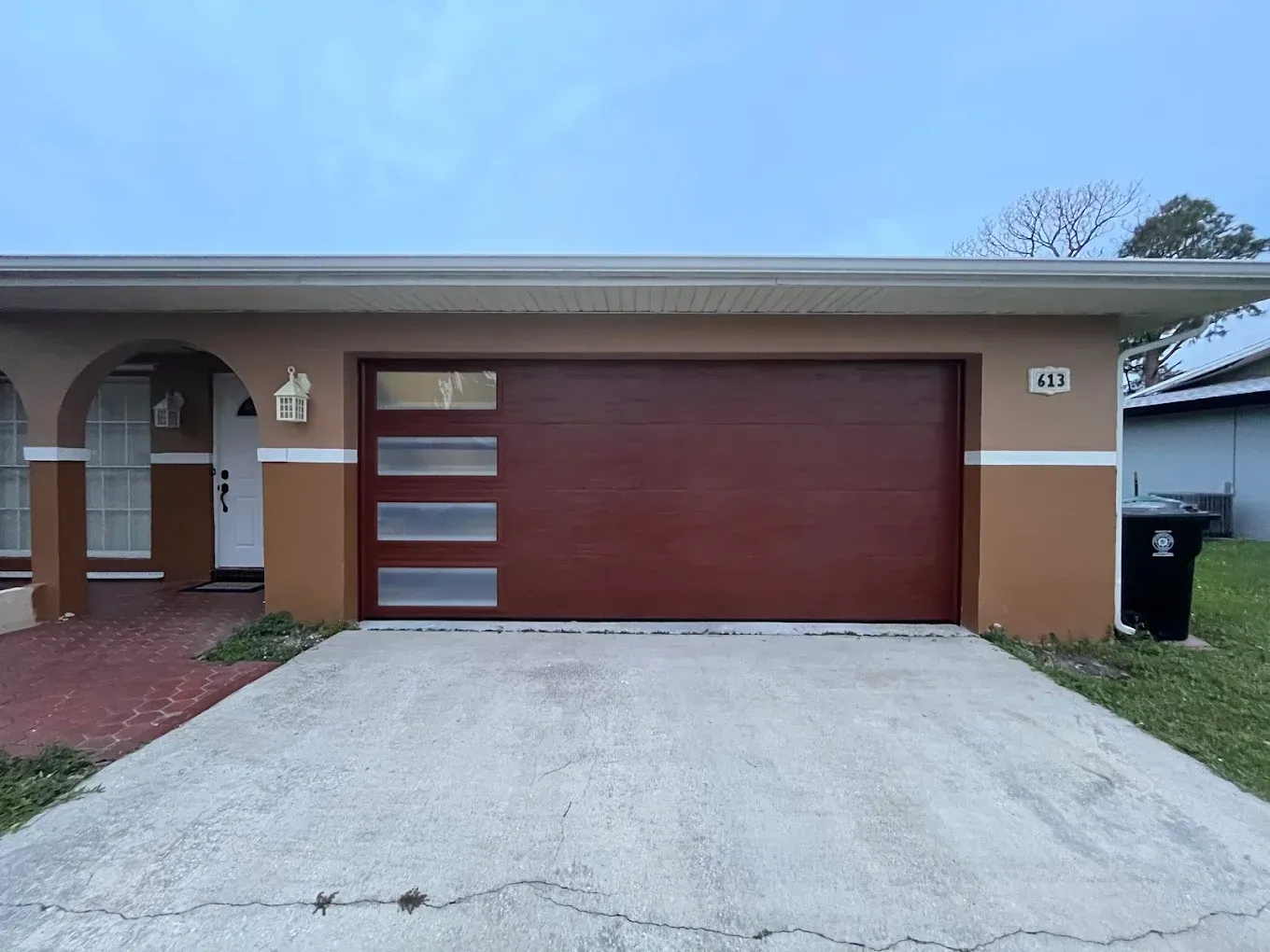 A tan house with a reddish-brown garage door featuring four horizontal frosted glass panels, next to a white front door.