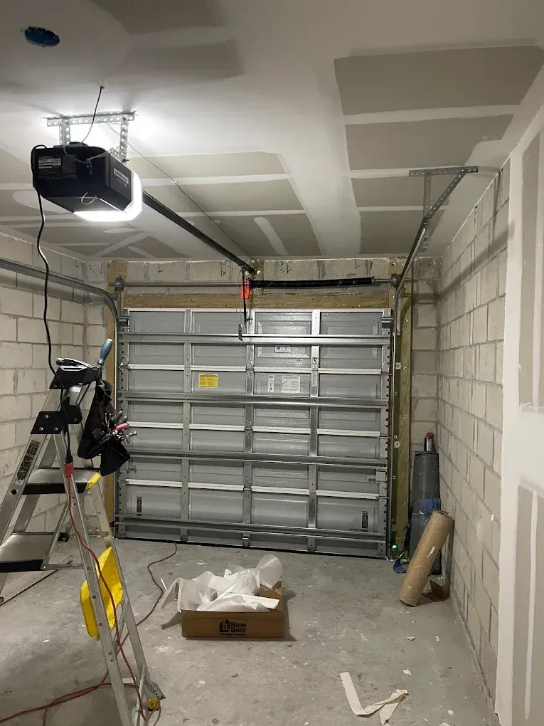 A garage interior with an installed overhead door opener, a metal garage door, and an A-frame ladder on a concrete floor.