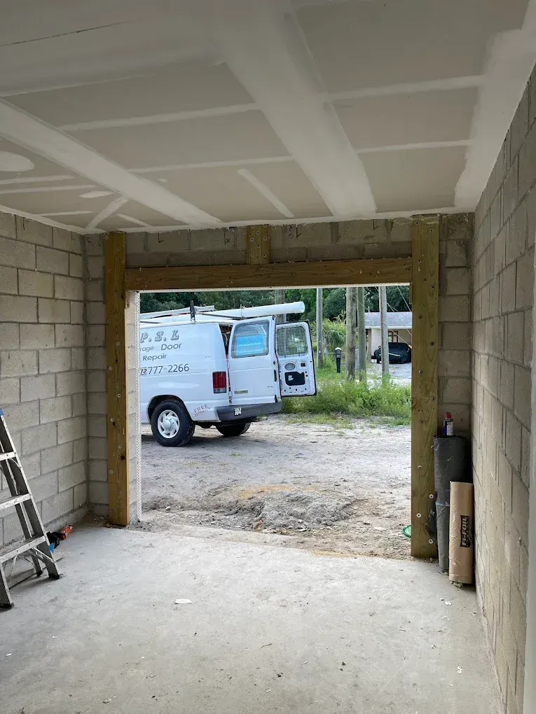 Interior view of a garage under construction, showing concrete block walls, a drywall ceiling, and a wooden door frame.