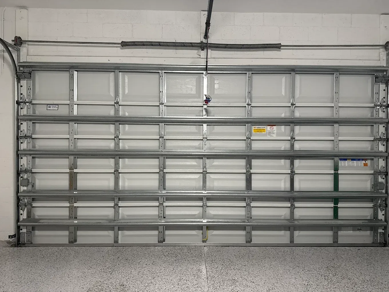 Interior view of a white, multi-panel residential garage door with steel horizontal reinforcements and tracks.