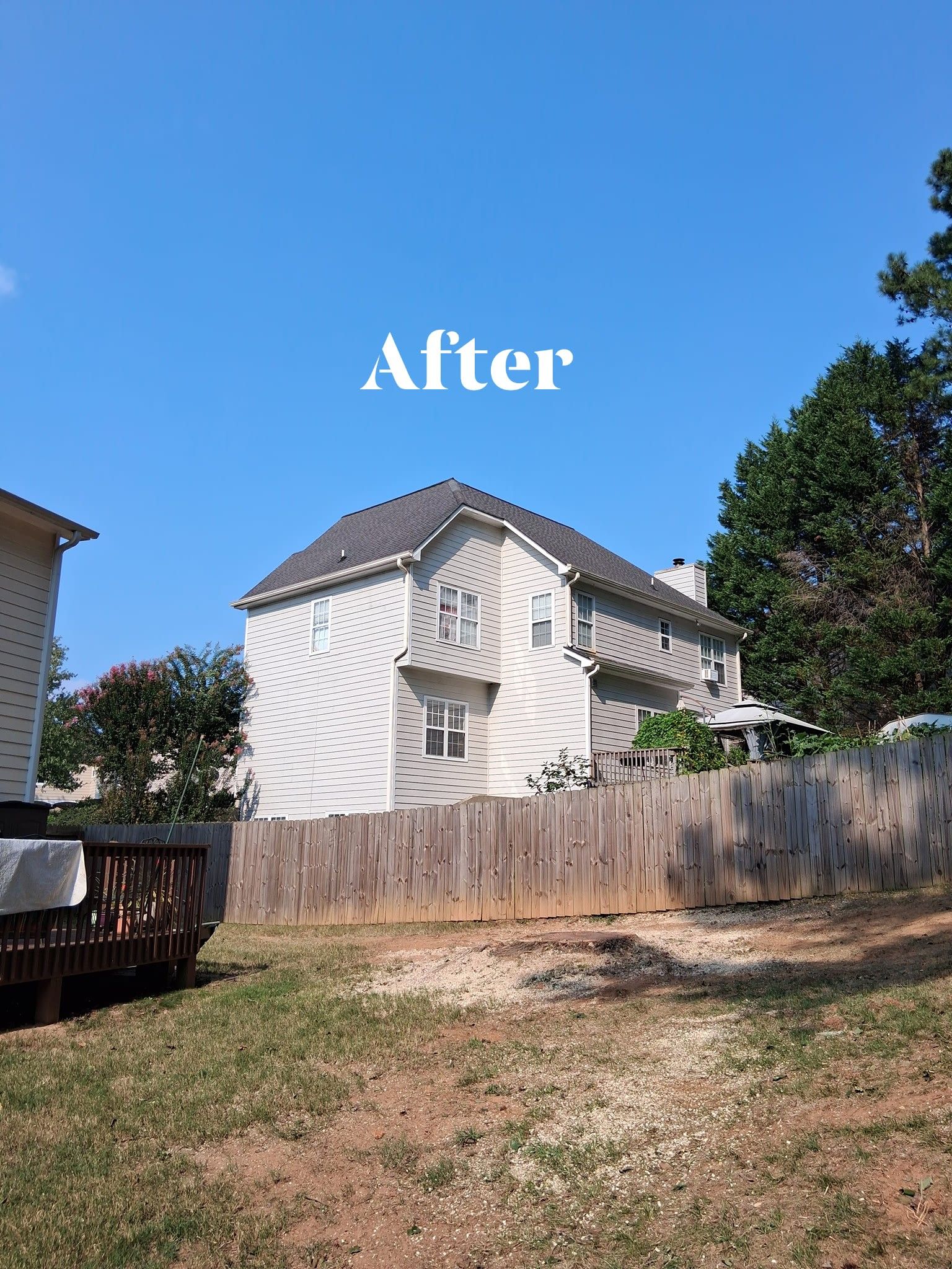 A two-story house with a grey roof, visible behind a wooden fence, under a blue sky.