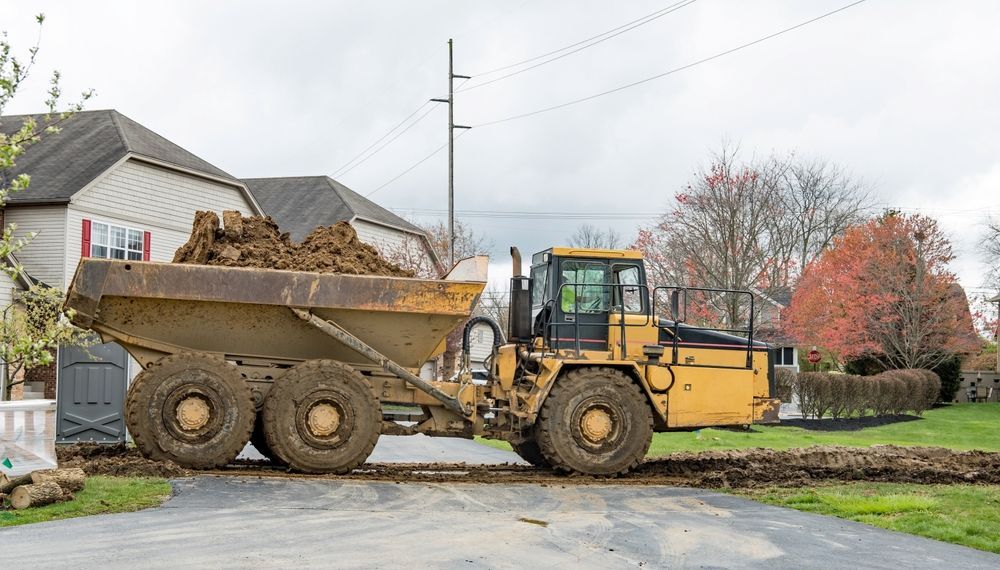 Yellow dump truck hauling dirt on a driveway near a house.