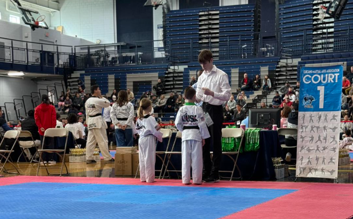 a group of children are standing on a karate mat in a gym .