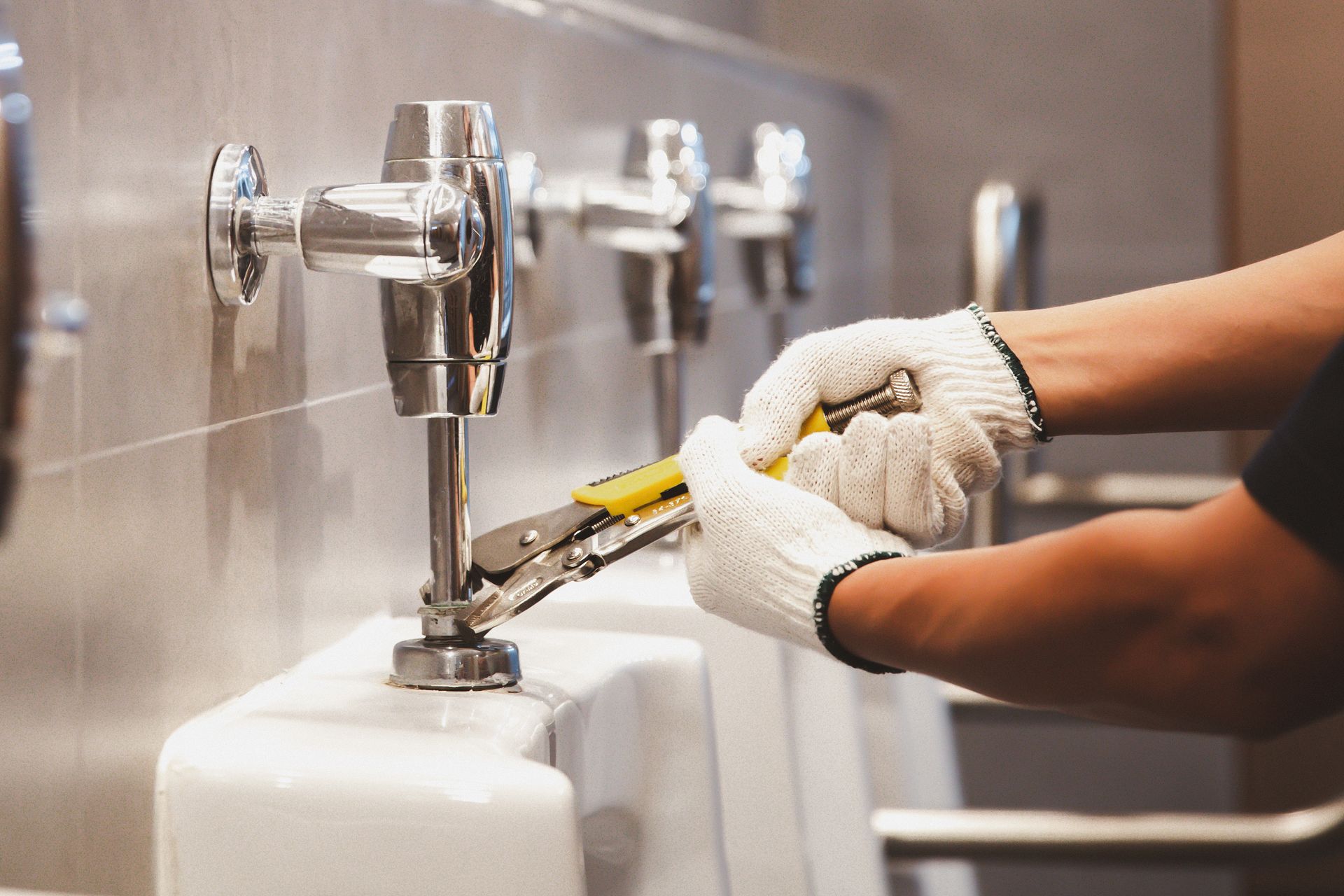 A man is fixing a urinal in a bathroom with a wrench.