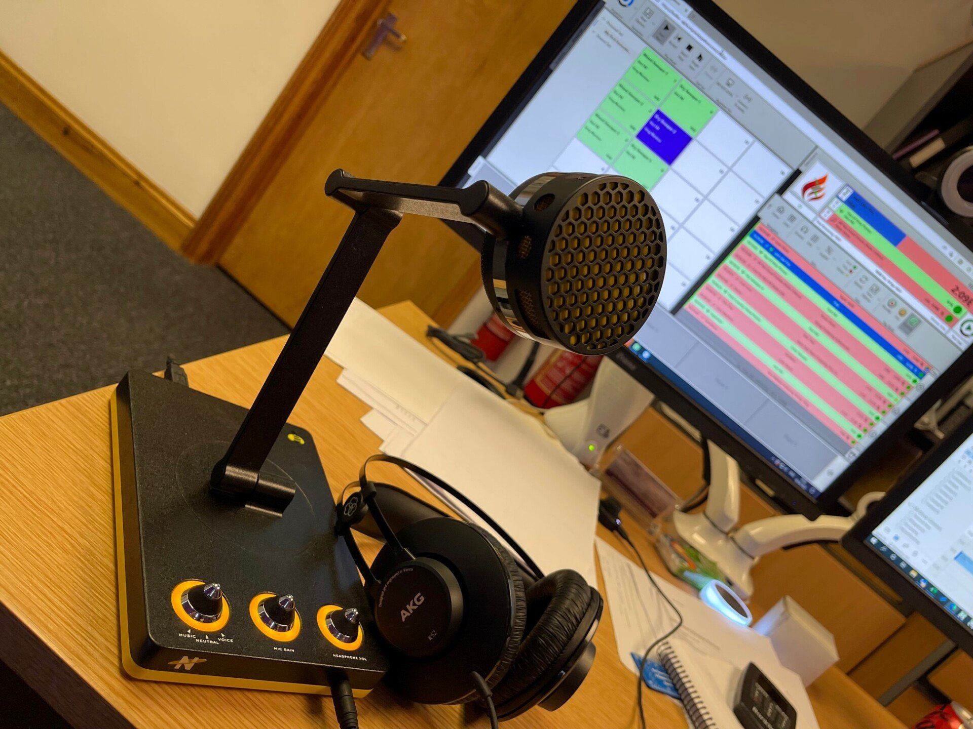 A microphone and headphones sit on a desk in front of a computer monitor