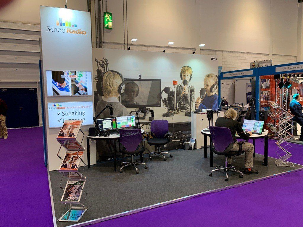 A group of people are sitting at desks in a room with purple carpet.