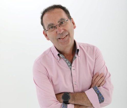 A man wearing glasses and a pink shirt with his arms crossed
