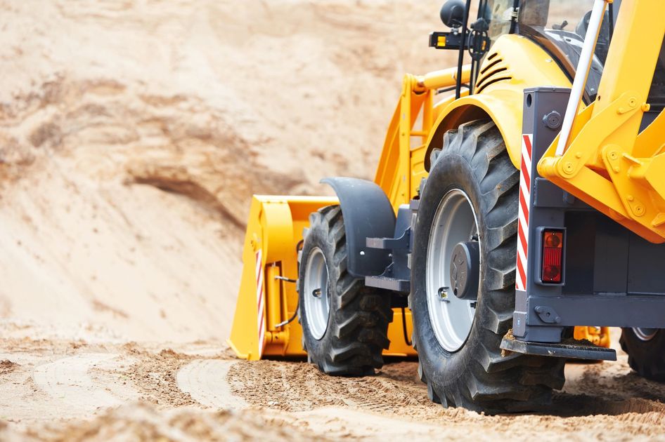 Una pala meccanica gialla e un autocarro ribaltabile sono al lavoro in un cantiere sabbioso.