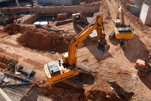 Cantiere edile con due escavatori gialli che scavano terra vicino a trincee e cumuli di terra.