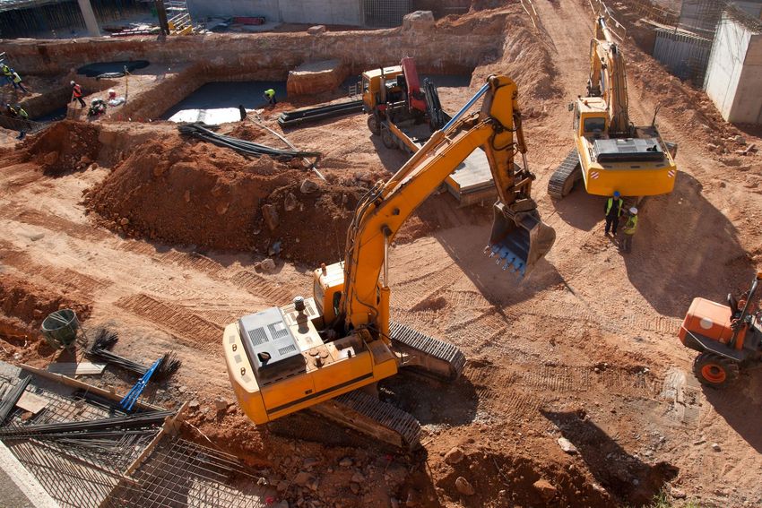 Cantiere edile con due escavatori gialli che scavano terra vicino a trincee e cumuli di terra.