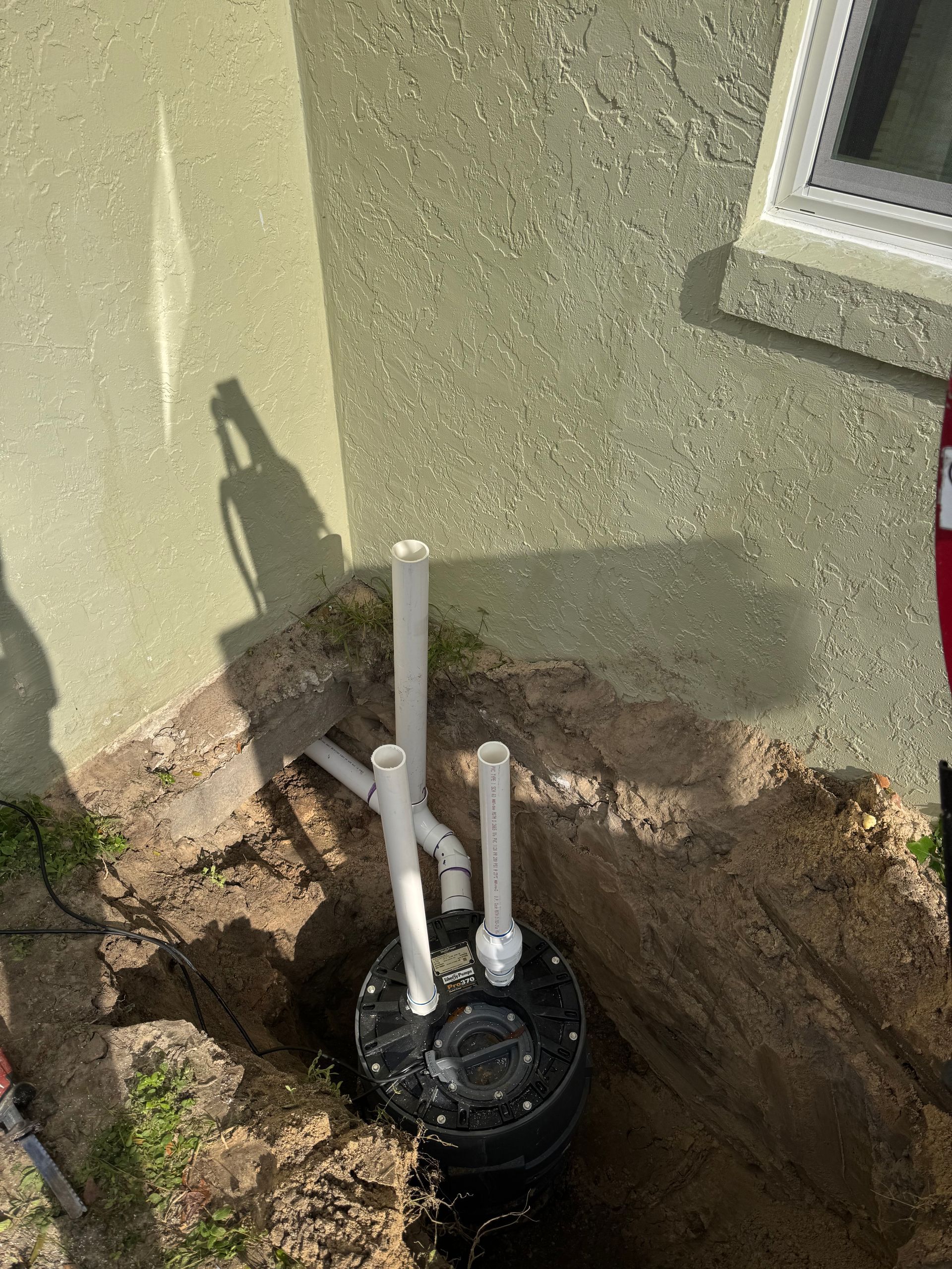 A drain pipe is being installed in the dirt in front of a house.