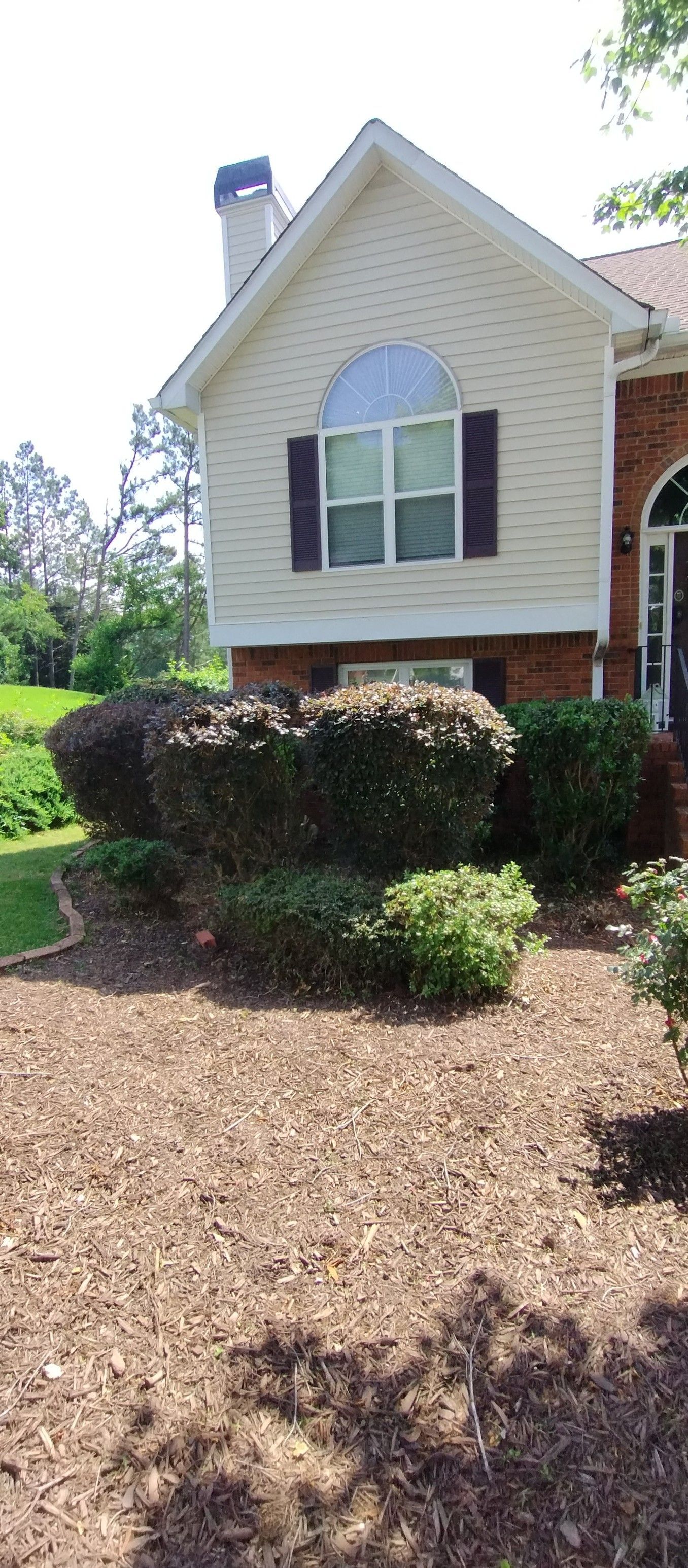 A suburban house exterior with light-colored siding, brick accents, arched windows, and manicured shrubs in the yard. A suburban house exterior with light-colored siding, brick accents, arched windows, and manicured shrubs in the yard.