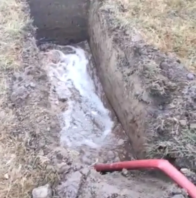 A red hose is coming out of a hole in the ground.