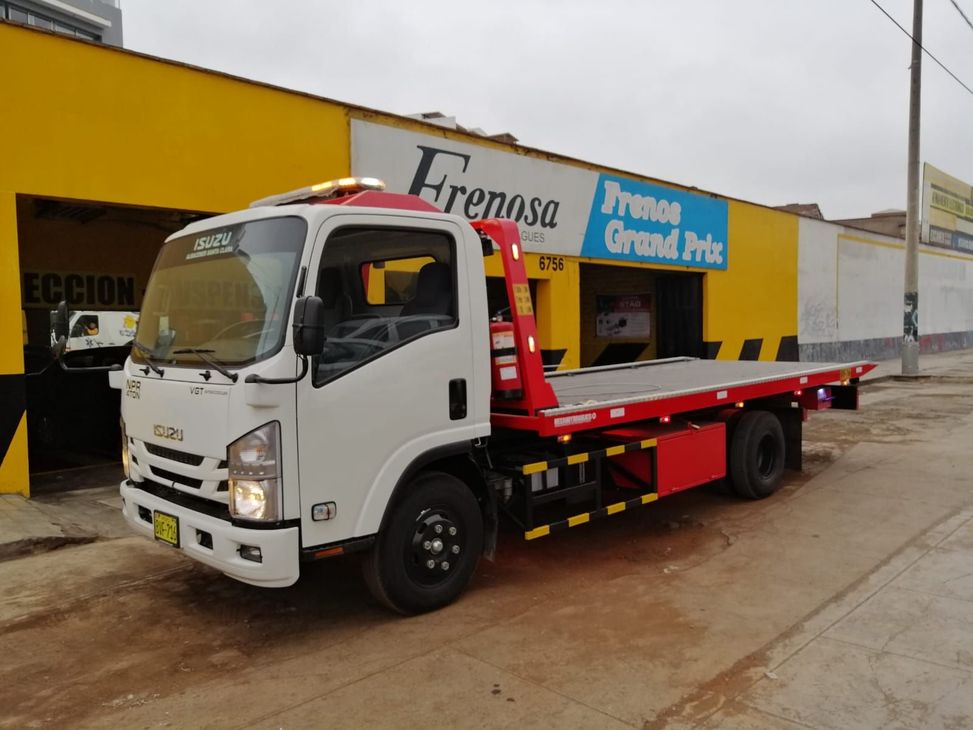 Una grúa de plataforma blanca estacionada frente a un edificio amarillo con un letrero azul.