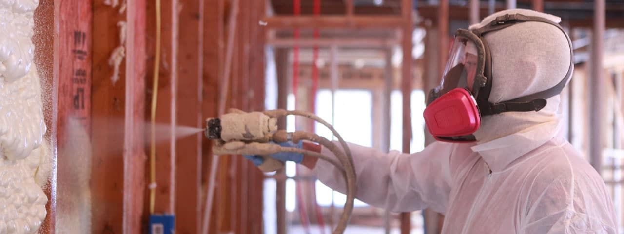 A man in a protective suit is spraying foam on a wall.