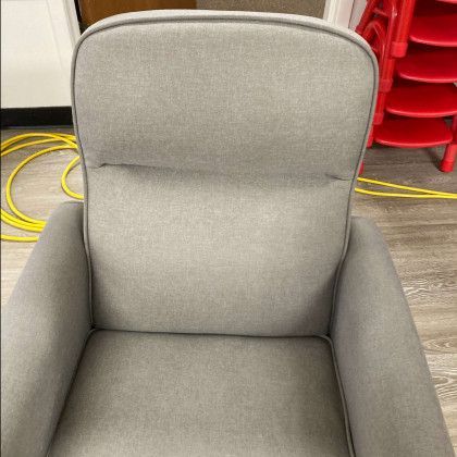 A grey chair is sitting on a wooden floor next to a stack of red chairs.