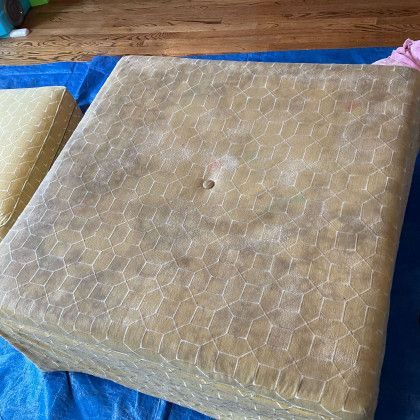 A dirty ottoman is sitting on top of a blue tarp on a wooden floor.