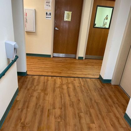 A hallway with wooden floors and a door in a hospital.
