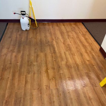 A spray bottle is sitting on a wooden floor next to a mop.