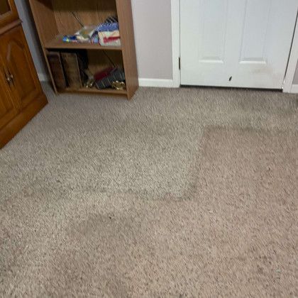 A room with a carpeted floor , a bookshelf , and a door.