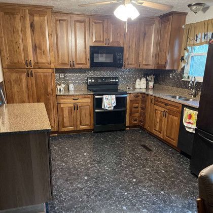 A kitchen with wooden cabinets , a stove , a microwave , a sink , and a refrigerator.