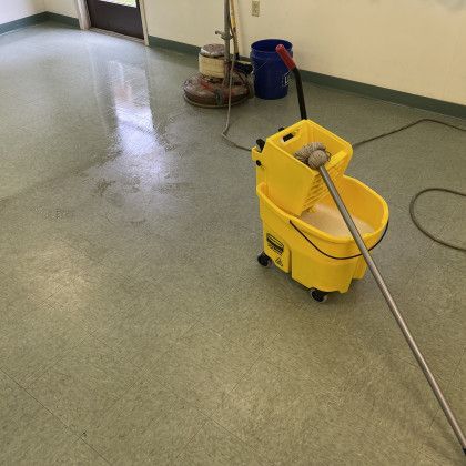 A yellow mop is sitting on the floor next to a vacuum cleaner.