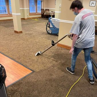 A man is cleaning a carpet with a vacuum cleaner.