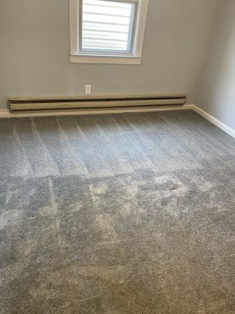 An empty room with a gray carpet and a window.