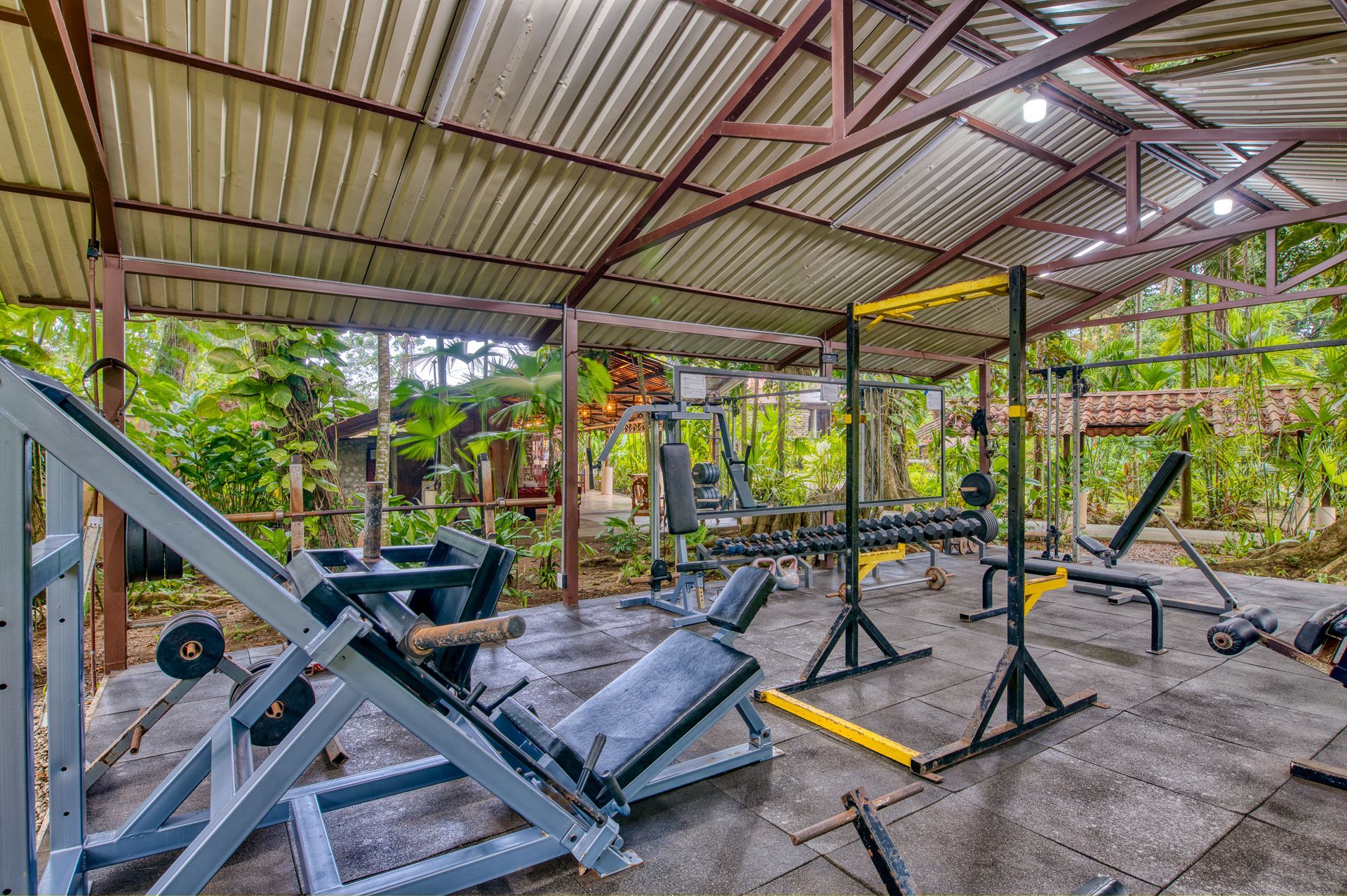 A gym filled with lots of exercise equipment under a roof.