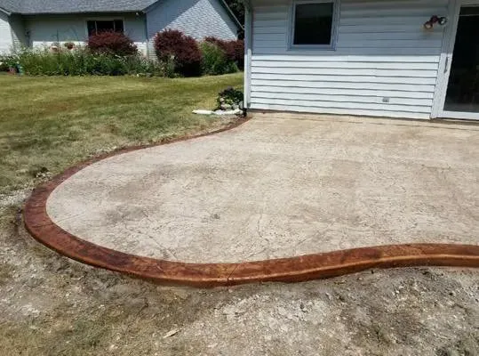 A concrete patio with a wooden border in front of a house