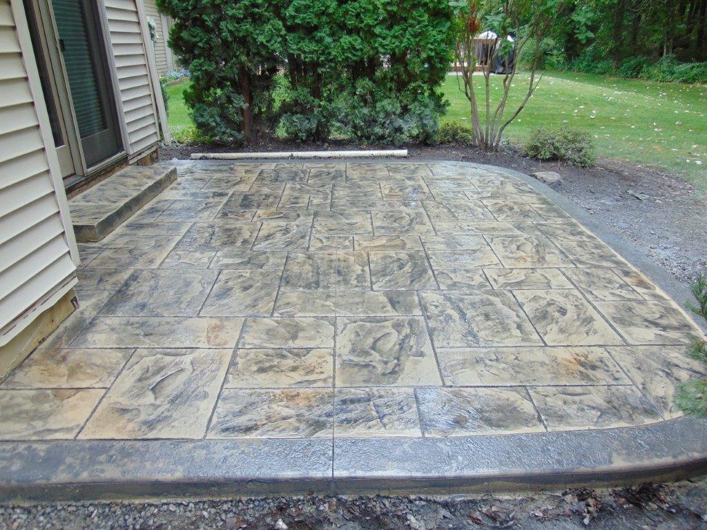 A textured concrete patio in front of a house with trees in the background