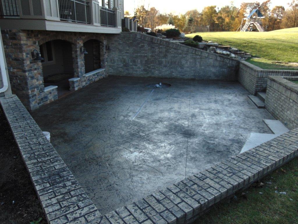 A large concrete patio with a stone wall and stairs in front of a house
