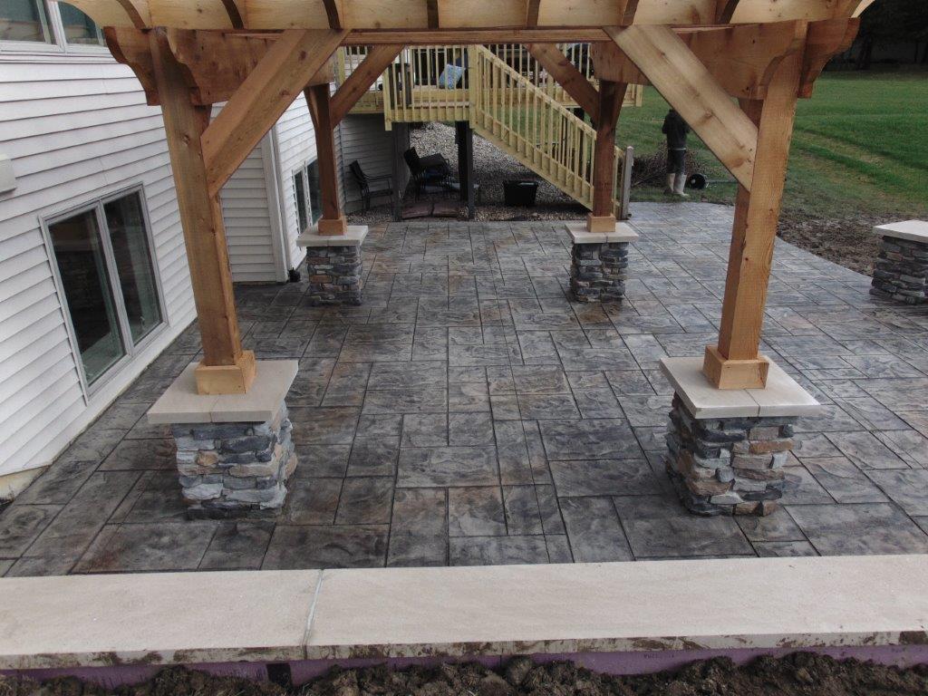 A patio with a wooden pergola and stone pillars