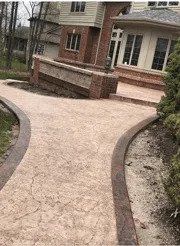 A concrete walkway leading to a house with a brick wall
