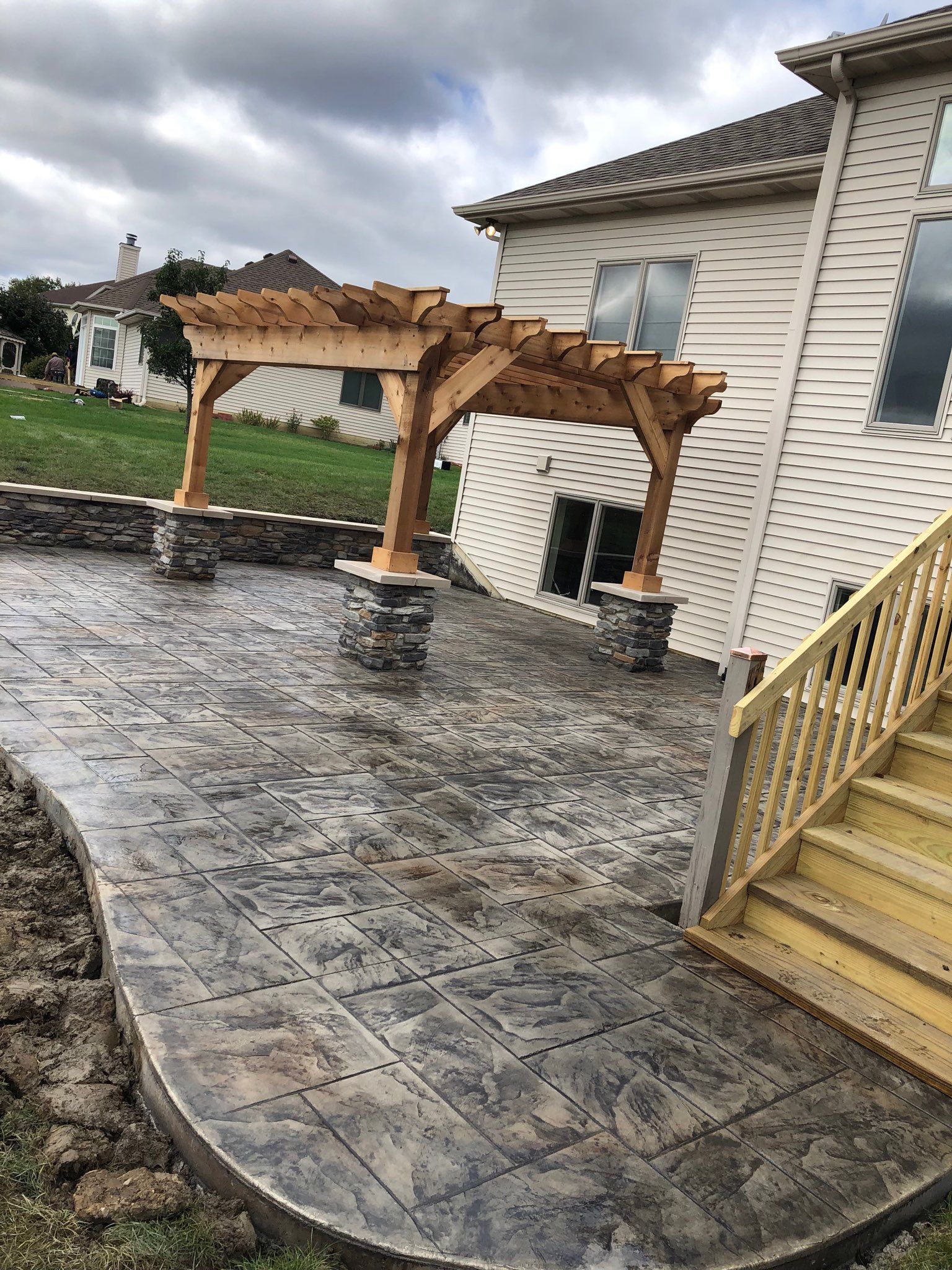 A patio with a wooden pergola and stairs in front of a house