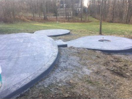 A concrete patio with a fire pit in the middle of a lush green field