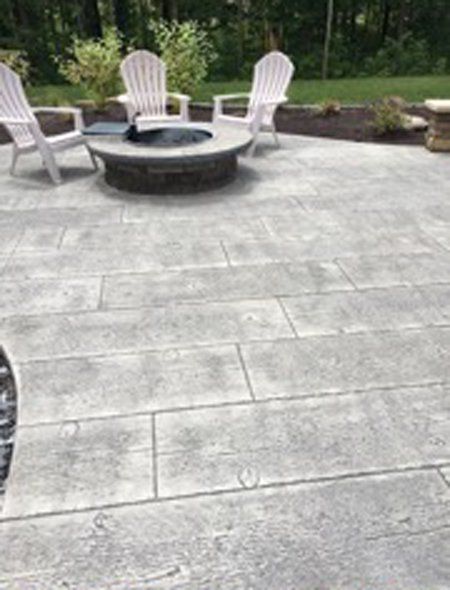 A nice concrete patio with a fire pit and chairs on it