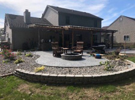 A patio with a fire pit and chairs in front of a house